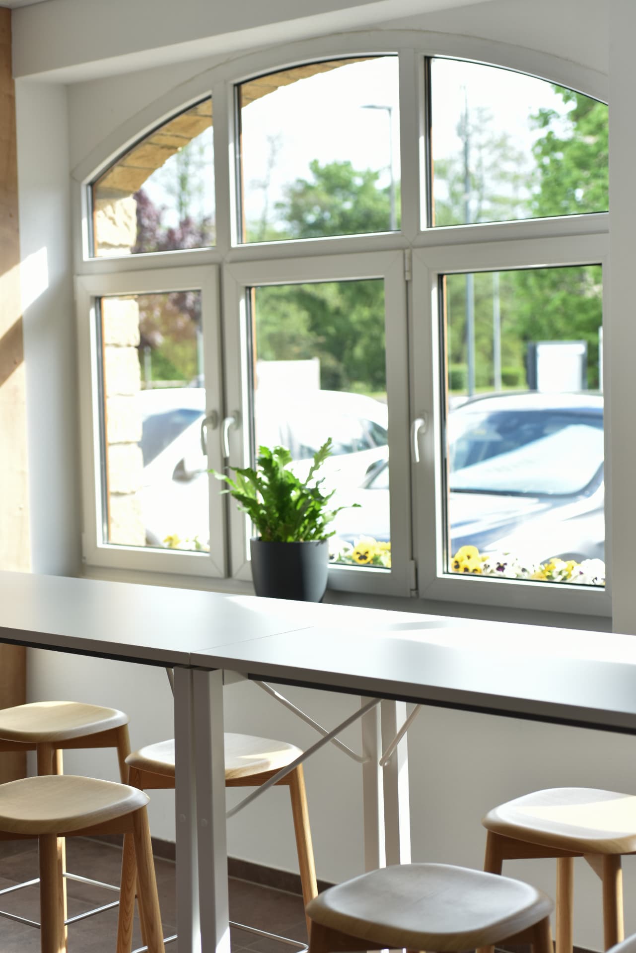 Sunlit coworking area with a long white high-top table and wooden stools